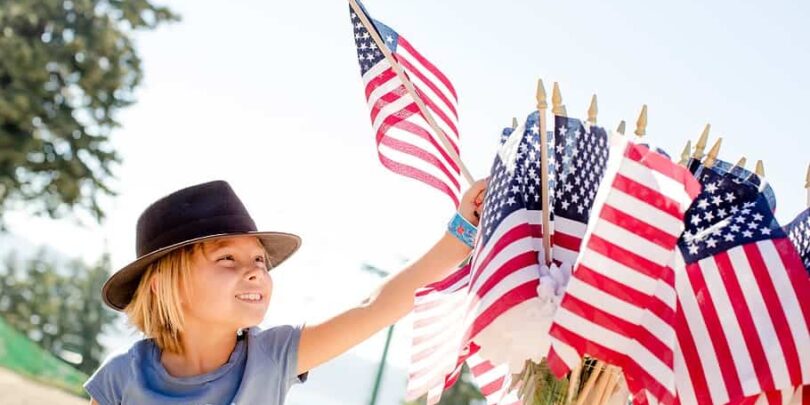 Photo of child reaching for a US flag for post about Independence Day 2023 - Toward a more perfect union